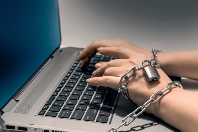 Hands,Shackled,In,Chains,Typing,On,A,Laptop,Keyboard.,The Individual Shackled to a laptop to show online gambling addiction
